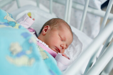 Sleeping newborn baby in bed of maternity birth clinic hospital. Beautiful portrait of little child girl 3 days, one week old.