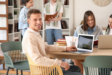 Male student studying with laptop at table in library
