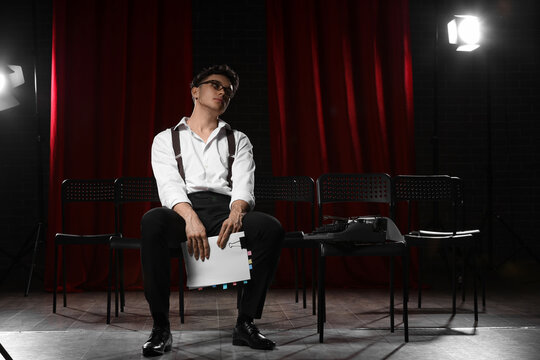 Tired male screenwriter with scenario sitting in chair on scene