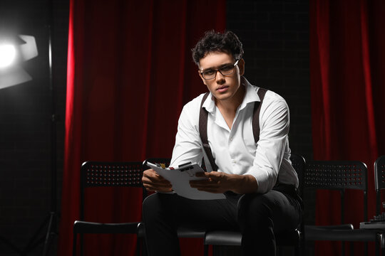 Male screenwriter with scenario sitting in chair on scene