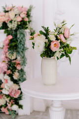 Bouquet of white and pale pink ranunculus and peonies in a ribbed ceramic vase sitting on a small white round table, with blurred floral decor in the classic white and pink background
