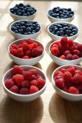 Bowls of fresh blueberries and raspberries arranged on a wooden surface nicely