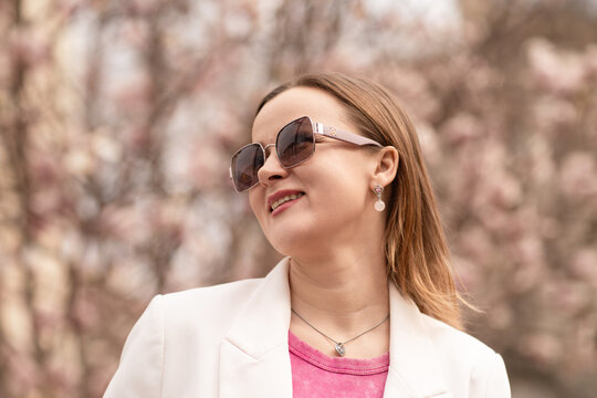 Woman Sunglasses Blossom: Smiling woman in spring with jacket, posing outdoors during the day surrounded by pink blossoms.