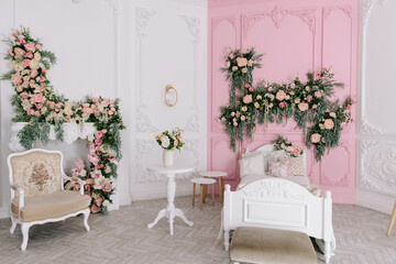 Elegant interior with pink and white walls featuring elaborate stucco and luxurious flower arrangements, showcasing a small bed and decorative side tables