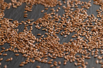 flax seeds scattered on slate, light brown flax seeds scattered on black slate surface