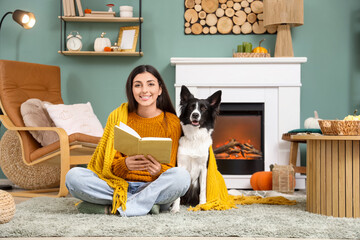 Young woman with plaid and cute Border Collie dog reading book at home on autumn day