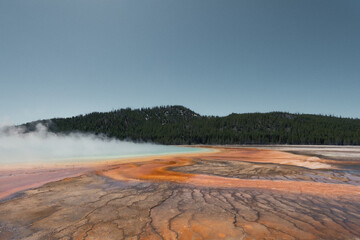 Vibrant geothermal basin with colorful bacterial mats and rising steam.