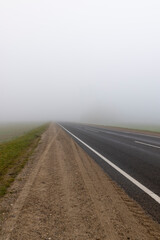 paved road in the autumn in cloudy weather with thick fog, highway with poor visibility due to fog