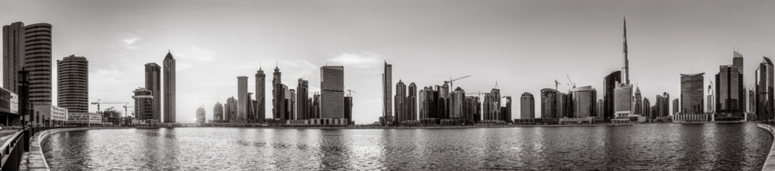 Monochrome city skyline with tall skyscrapers reflecting on calm water under a cloudy sky, Dubai Marina bay UAE