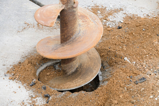 Construction workers are repairing a road by excavating and drilling the pavement to fill underground voids with specially mixed concrete. Heavy machinery and roadwork safety cones are visible.