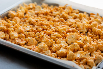 raw cauliflower and chickpeas seasoned with paprika in tray ready to bake