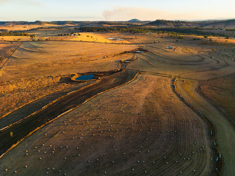 A golden brown coloured paddock dotted with hay bales and small dams