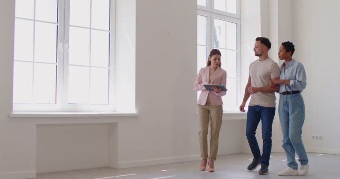 Female cheerful real estate agent showing new apartment to young happy couple planning to buy property. Man and woman talking with realtor in new house. Real estate market concept. 4k video.