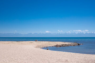 lonely wooden bench on sandy beach facing calm blue sea, Issyk Kul, Kyrgyzstan, horizontal view
