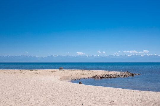 lonely wooden bench on sandy beach facing calm blue sea, Issyk Kul, Kyrgyzstan, horizontal view