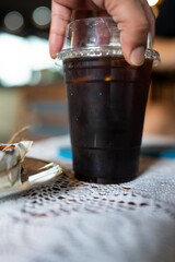 Close up view of cold brewed black coffee in a plastic cup put on white desk and hand picking up