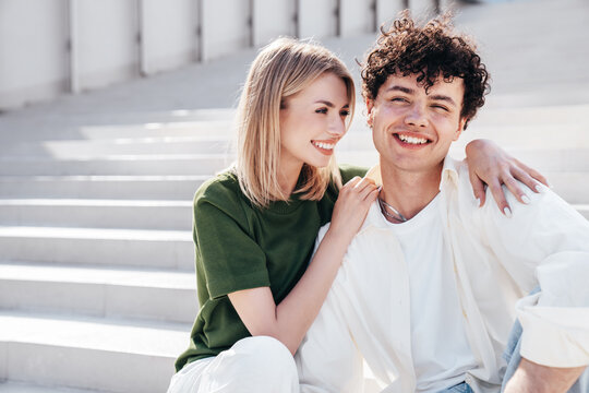 Smiling beautiful woman and her handsome boyfriend. Couple in casual summer clothes. Happy cheerful family. Female and man having fun. They posing in the street in sunny day. sit at stairs
