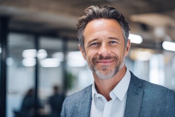 Obraz premium Confident mid aged business man executive standing in a modern office environment with a bright smile during a productive workday