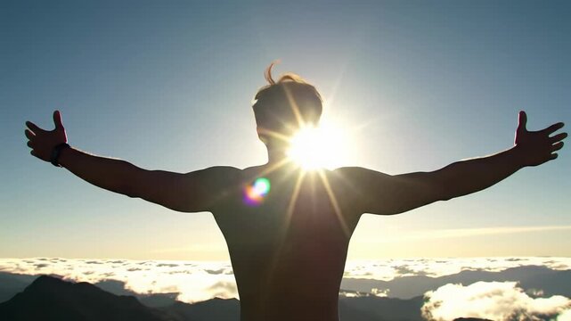 A lone man silhouetted against golden hour sunrise on mountain peak, raising arms amidst sea of clouds. Crane lift, dolly push to low-angle video, anamorphic flares. Concept of ultimate liberation
