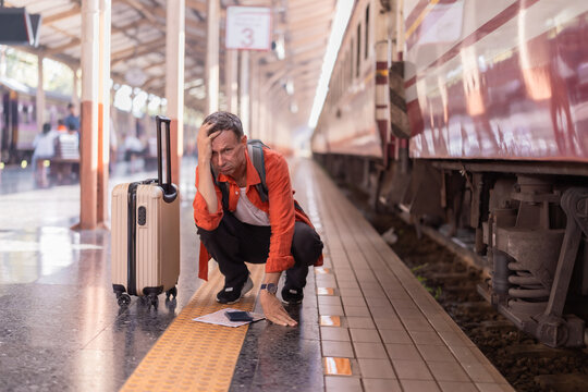 Traveler feeling stressed and hopeless on a train station platform, holding head while a train departs, representing missed connection and travel problems