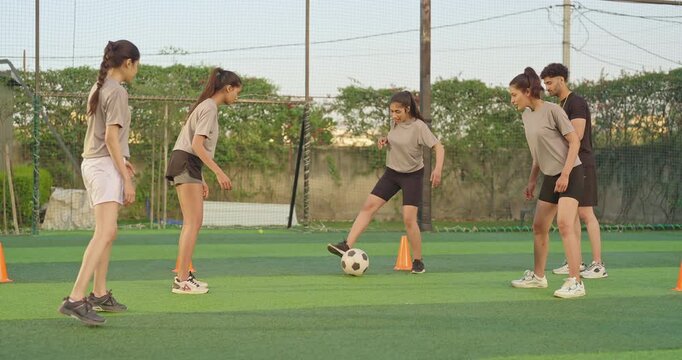 Indian young adult man coach blow whistle woman lady learn play game kick to soccer ball male guy trainer leader training to sports teen girl group team enjoy casual football match day at ground place