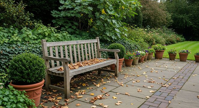 Wooden park bench covered in autumn leaves on garden stone patio