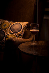 The surroundings are dark and atmospheric, which is typical for a cozy bar or cocktail lounge. A patterned cushion and a round wooden table contribute to the warm, inviting atmosphere.