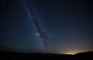 Fototapeta premium Night sky with stars above mountain terrain. Starry space scene with visible meteors and constellation. Dark astrophotography landscape against milky way. Concept of explore cosmos and distant galaxy.