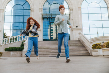 Happy brother and sister running playfully down steps of glass urban building