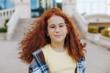 Confident redhead teenage girl with glasses posing outdoors in casual outfit