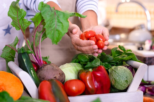Close-up of two woman hands holding fresh cherry tomatoes over a table full of colorful organic vegetables. Concepts of healthy eating, sustainable lifestyle, vegetarian food, connection to nature