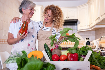 Happy senior woman and her adult daughter cooking together in a kitchen full of fresh vegetables preparing healthy food. Family connection, healthy eating, vegetarian lifestyle concept