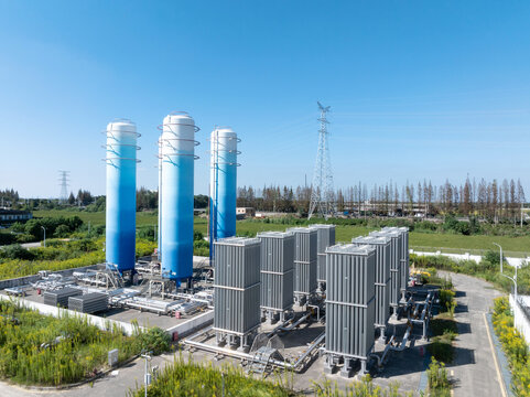 Industrial gas facility with blue towers, pipes, and power lines in rural area.