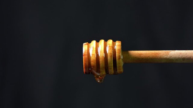 Honey dripping from a wooden dipper. Drop of golden liquid honey drips slowly from the wooden dipper. - Powered by Adobe