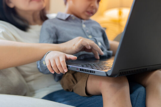 Happy Asian mom with her little son use laptop, playing video game on sofa at home. - Powered by Adobe