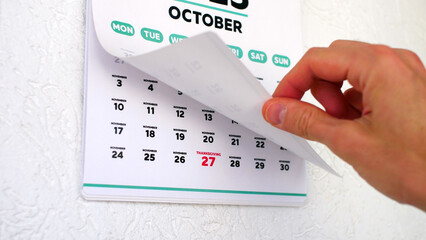 A male hand lifts October page of a wall calendar followed by the next one with the date of...