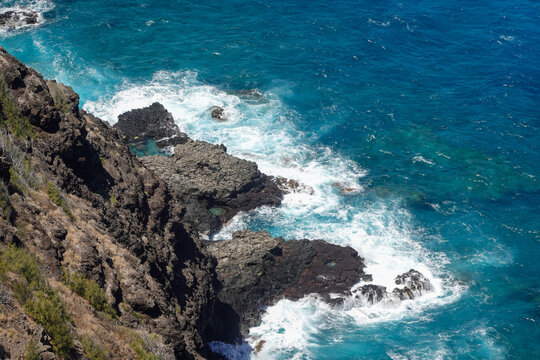 Vertical cliff face with turquoise surf pounding narrow rocky inlet below