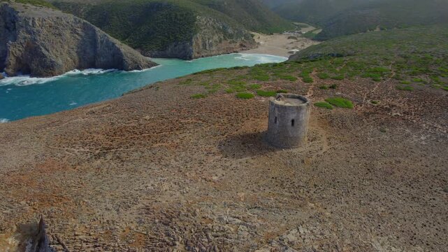 Aerial orbiting shot of the Spanish tower on a promontory overlooking Cala Domestica bay in Sardinia