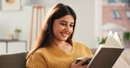 Coffee, reading book and woman in home for story, fantasy and morning beverage. Tea, literature and happy person on sofa in living room with drink, fiction and hobby for relax on weekend break