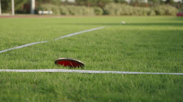 A throwing disc falling on the lawn of a sports field, filmed in slow motion