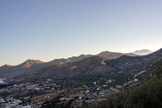 Peaceful mountain landscape in Crete, Greece, captured at golden hour. The warm evening sunlight softly illuminates the rugged hills and small white houses scattered across the valley