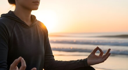 Woman meditating in a yoga pose with hands in mudra, facing the ocean at sunset, promoting wellness and mindfulness.