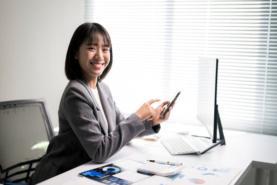 Asian businesswoman smiling holding smartphone working in office