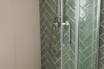 Silver Glass door handle of a glass partition shower unit. Bathroom glass door detail with bath tub in the background. Selective focus and soft light effect added.