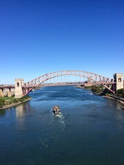 Naklejka premium Majestic Steel Arch Bridge Spanning River under Clear Blue Sky with Passing Boat