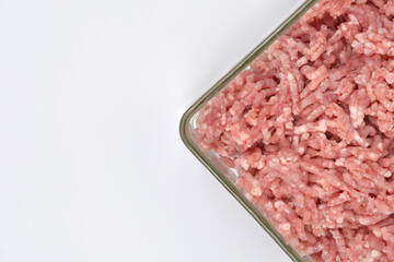 An overhead close-up of raw ground pork in a glass dish, positioned diagonally in the bottom right on a clean white background with copy space