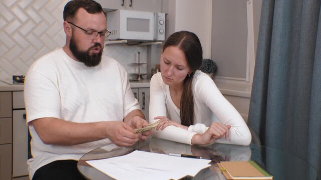 Concerned young couple carefully calculating domestic expenses at home kitchen table, reviewing financial challenges and struggling to manage limited household budget with remaining dollars