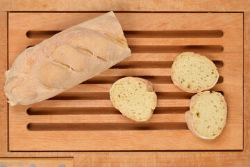A partial baguette loaf and three thick slices of bread are arranged on a light brown wooden cutting board with horizontal grooves