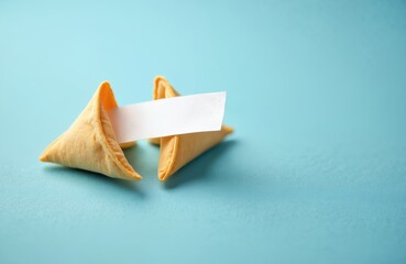 Two fortune cookies with blank paper message on light blue background. One cookie shows empty space for custom text. Dessert luck, future prediction, pleasant surprise. Use for New Year, wisdom