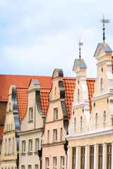 Colorful historic gabled houses with red tile roofs and ornate facades under a lightly clouded sky in an old town